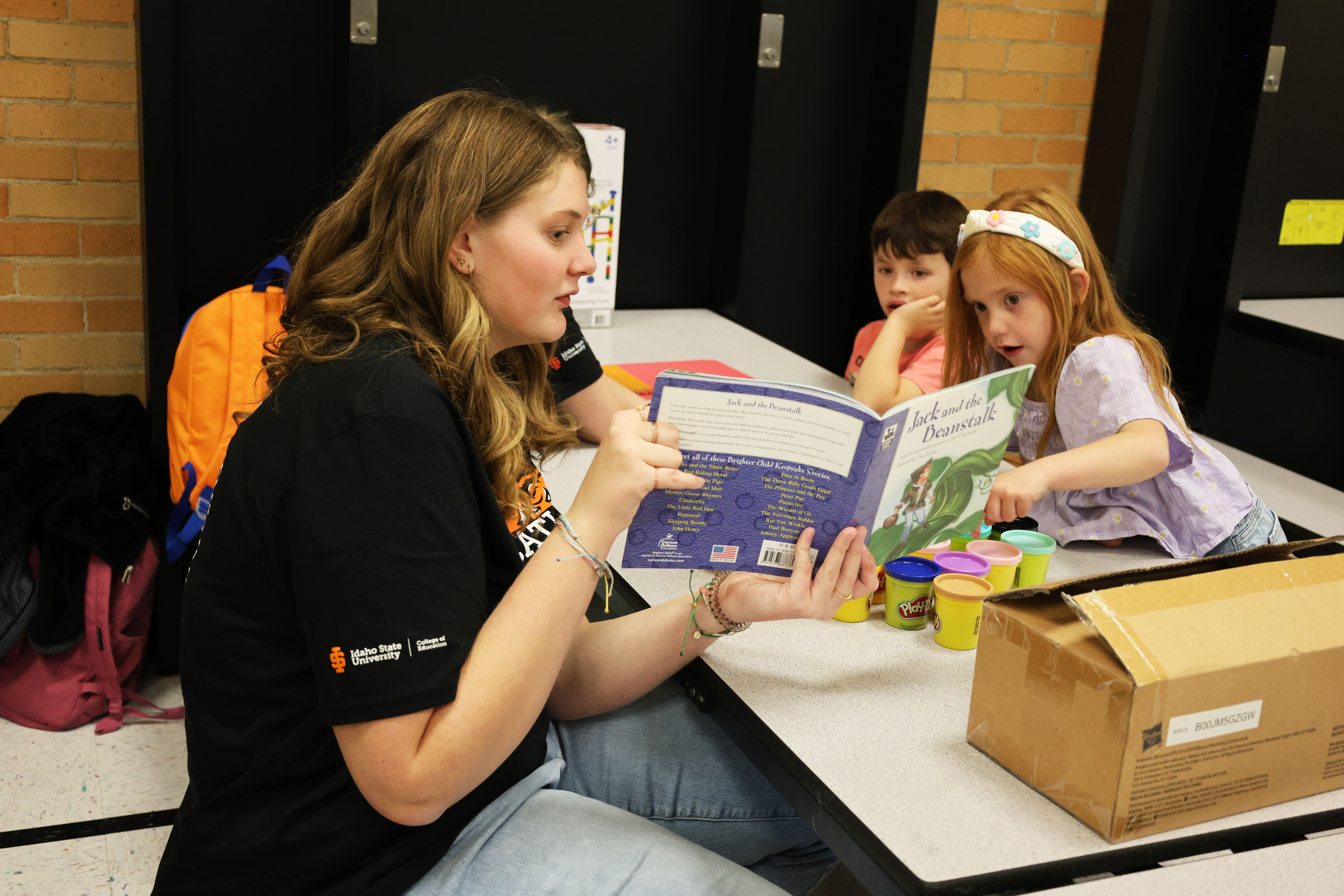 A student reading a book to two young students in an elementary school