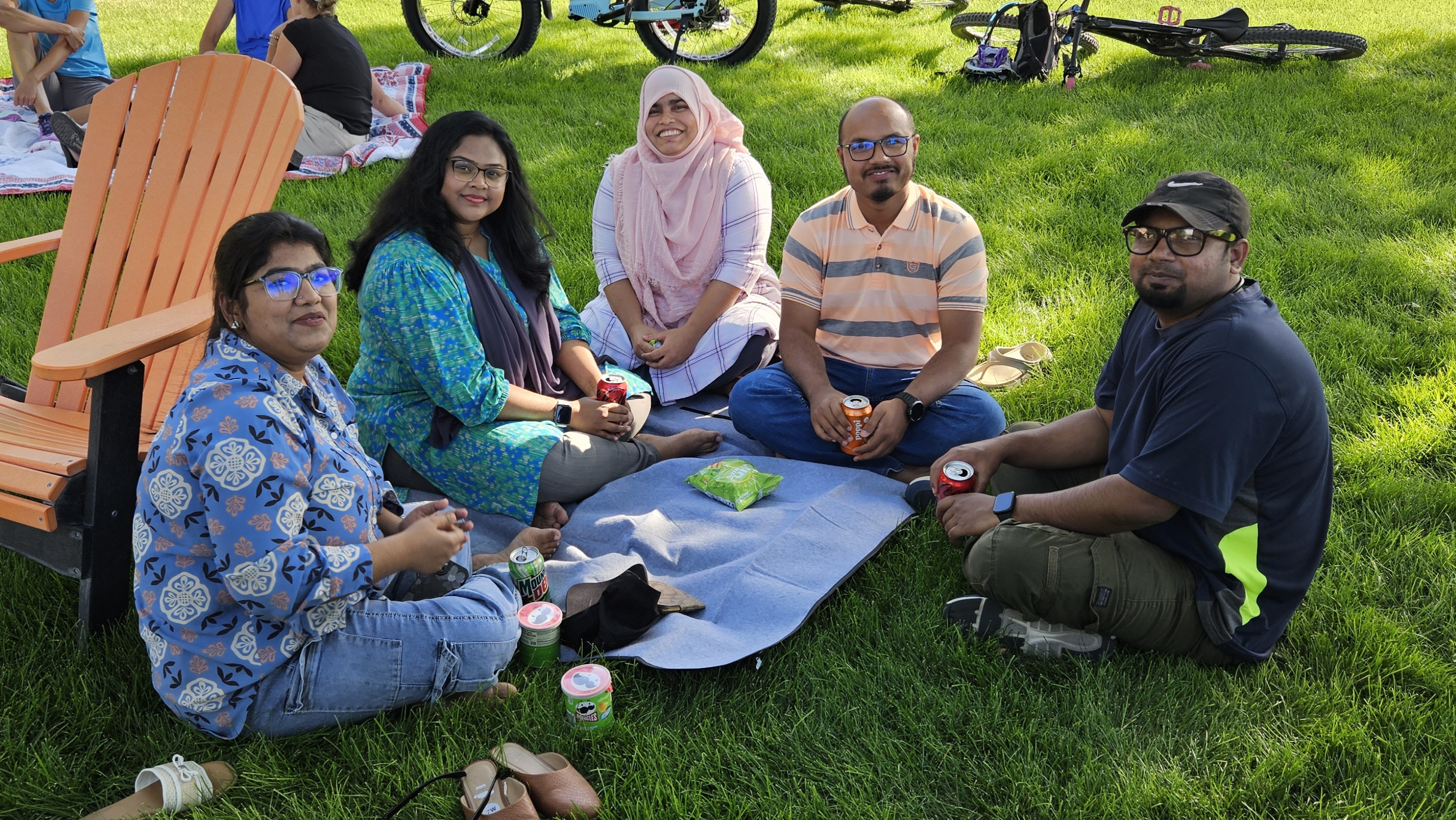 a group of five students sitting on the grass at Summer Nights with the Grad School and smiling for the camera