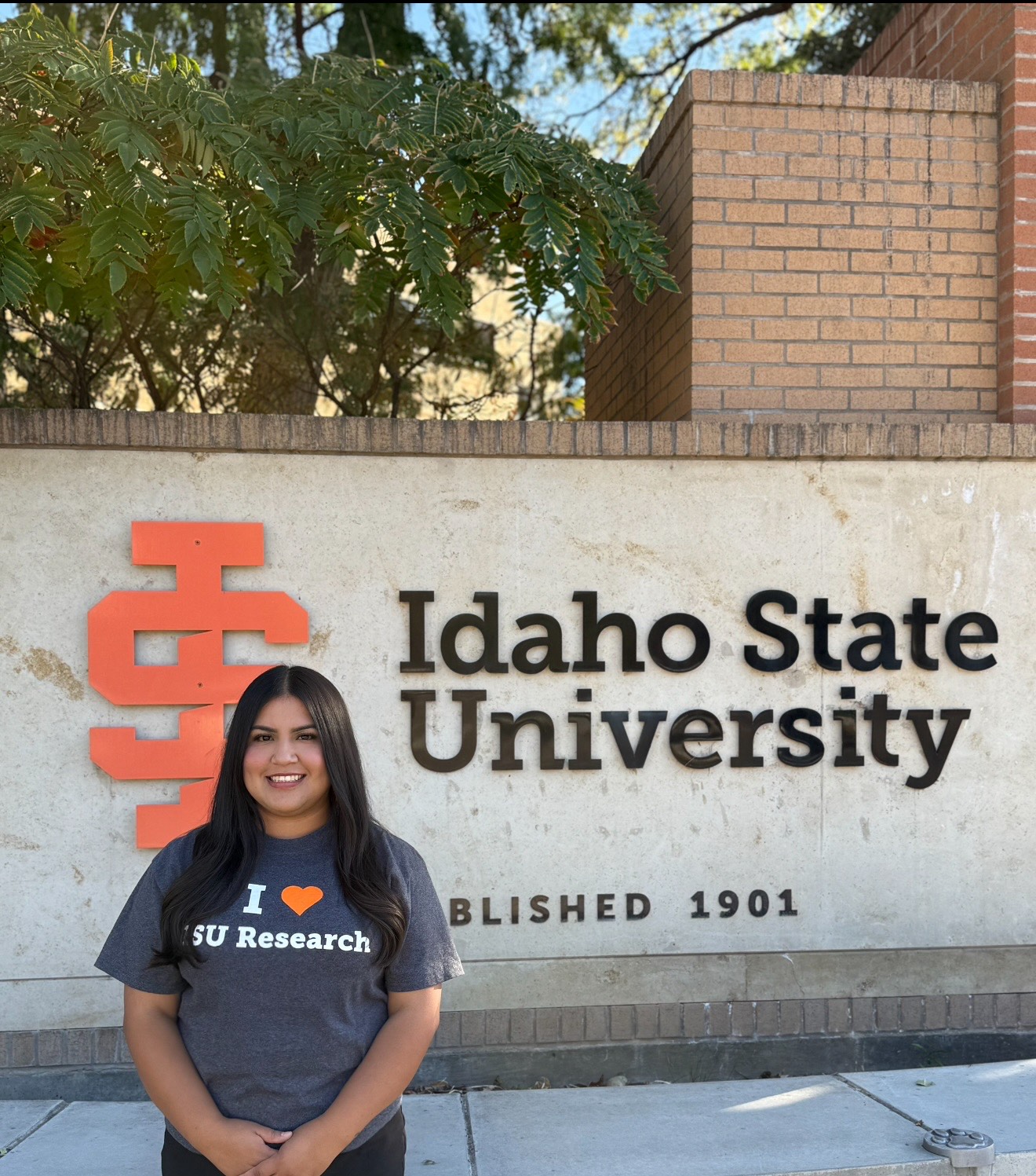 Student stands in front of Idaho State University sign wearing shirt that says I Love Research