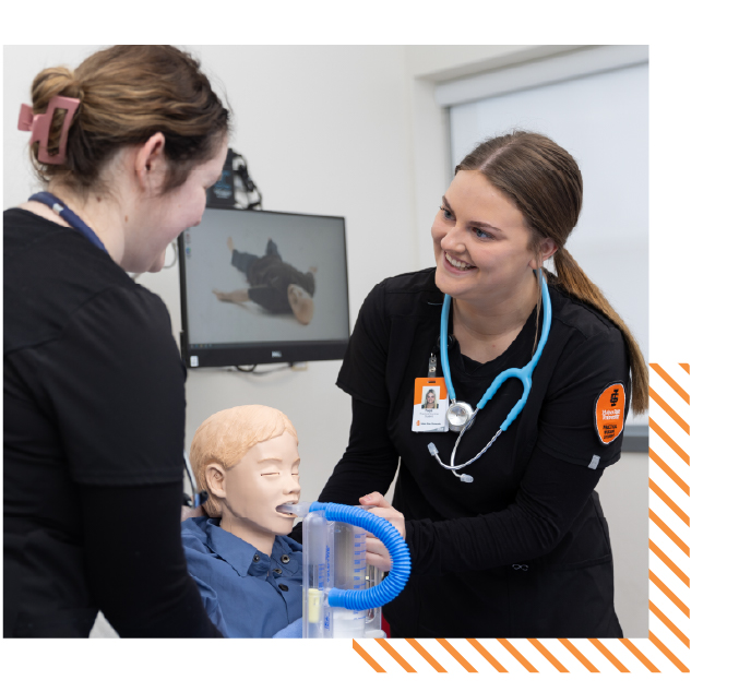Two college students in a healthcare classroom practice patient care using a medical training mannequin, representing hands-on learning and career-focused education in ISU’s bachelor’s degree programs.