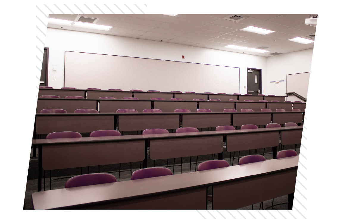 Tiered classroom at ISU Idaho Falls with rows of long tables and purple chairs facing the front of the room.