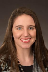 A woman with light skin tone, blue eyes, and brown hair. She is wearing a black and white sweater