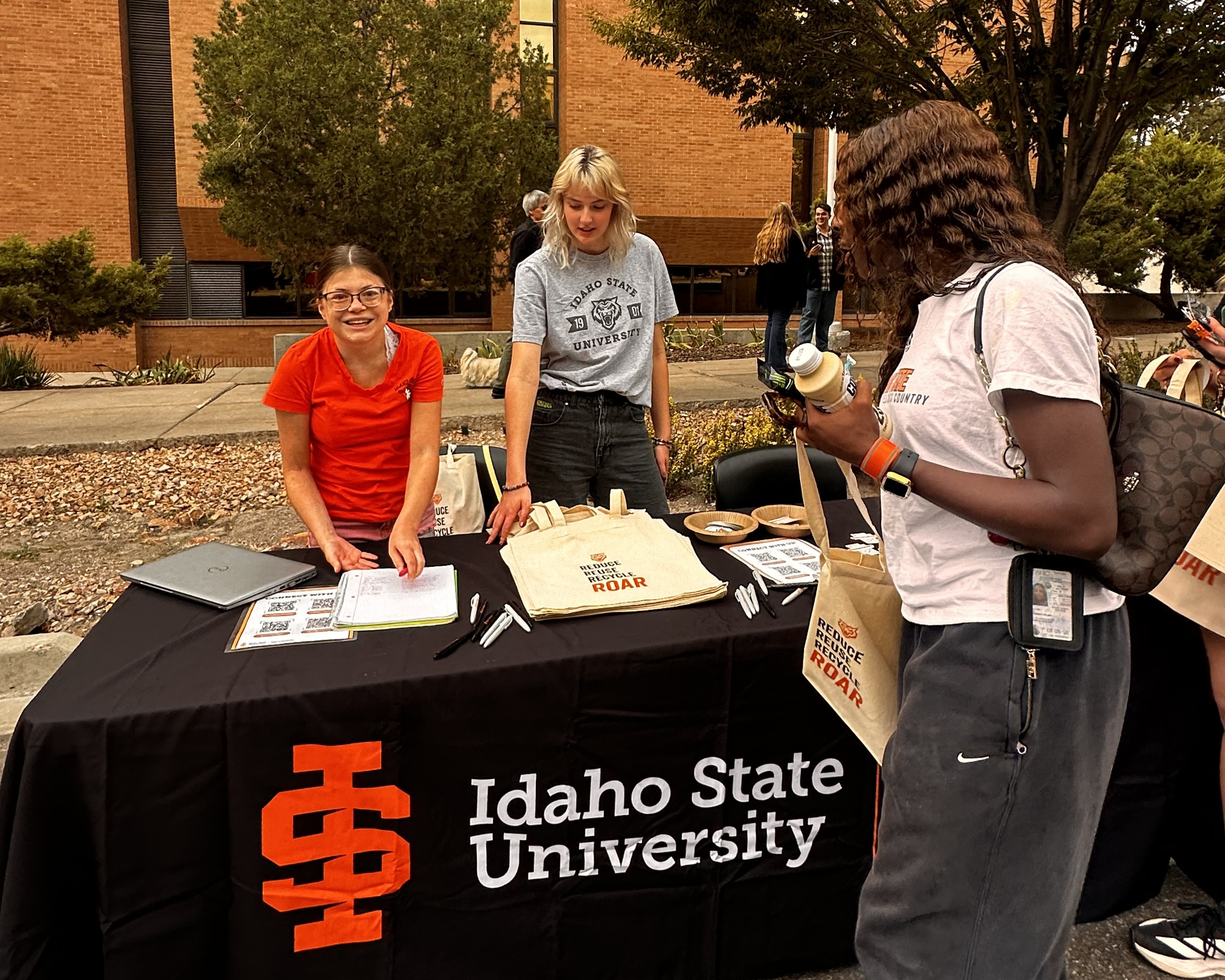 the sustainability club president and a sustainability intern behind a booth speaking to a student