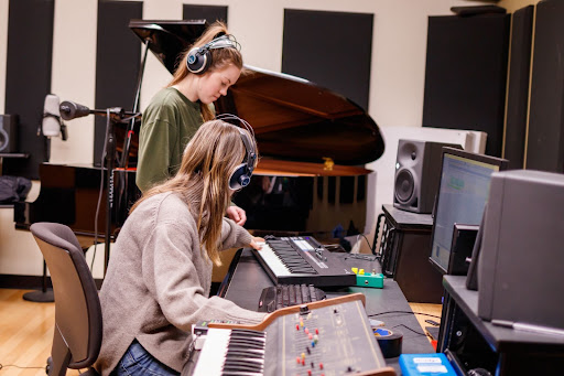 A student plays a piano while another one listens